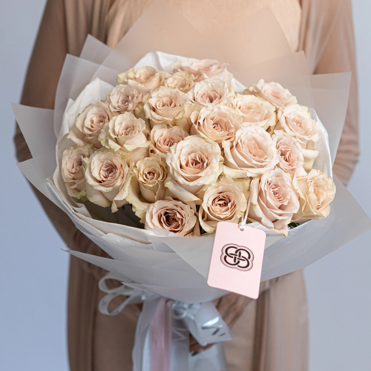 Champagne quicksand roses bouquet wrapped in white paper with pink brand tag and satin ribbon