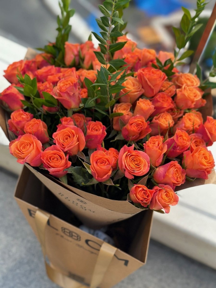 Vibrant coral-orange roses with green foliage arranged in brown kraft paper wrapping bouquet