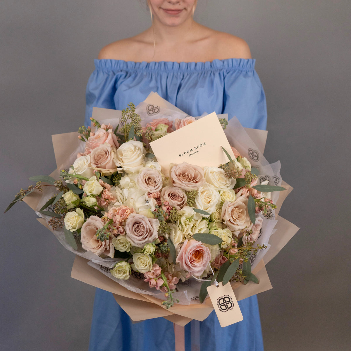 Large mixed rose bouquet in cream, blush pink and white with kraft paper wrapping held by woman in blue dress