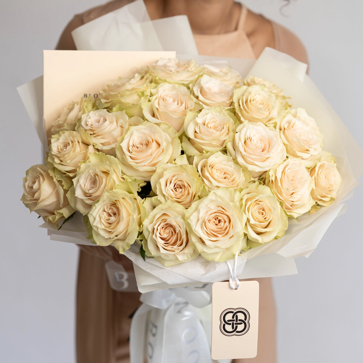 Elegant bouquet of 25 cream and peach roses wrapped in white tissue paper with gift tag