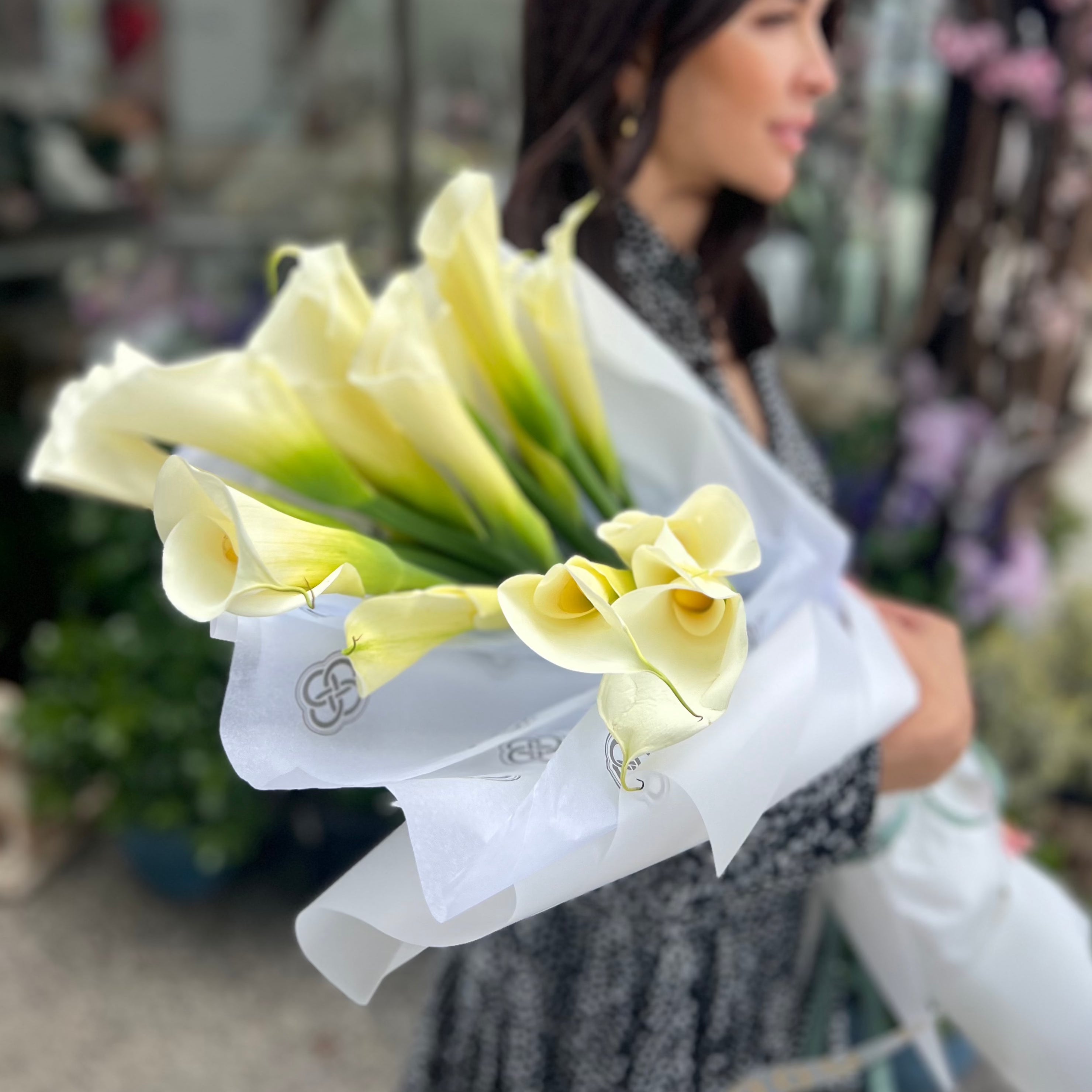 Cream white calla lily bouquet wrapped in tissue paper with gray ribbon held by woman in Los Angeles flower shop
