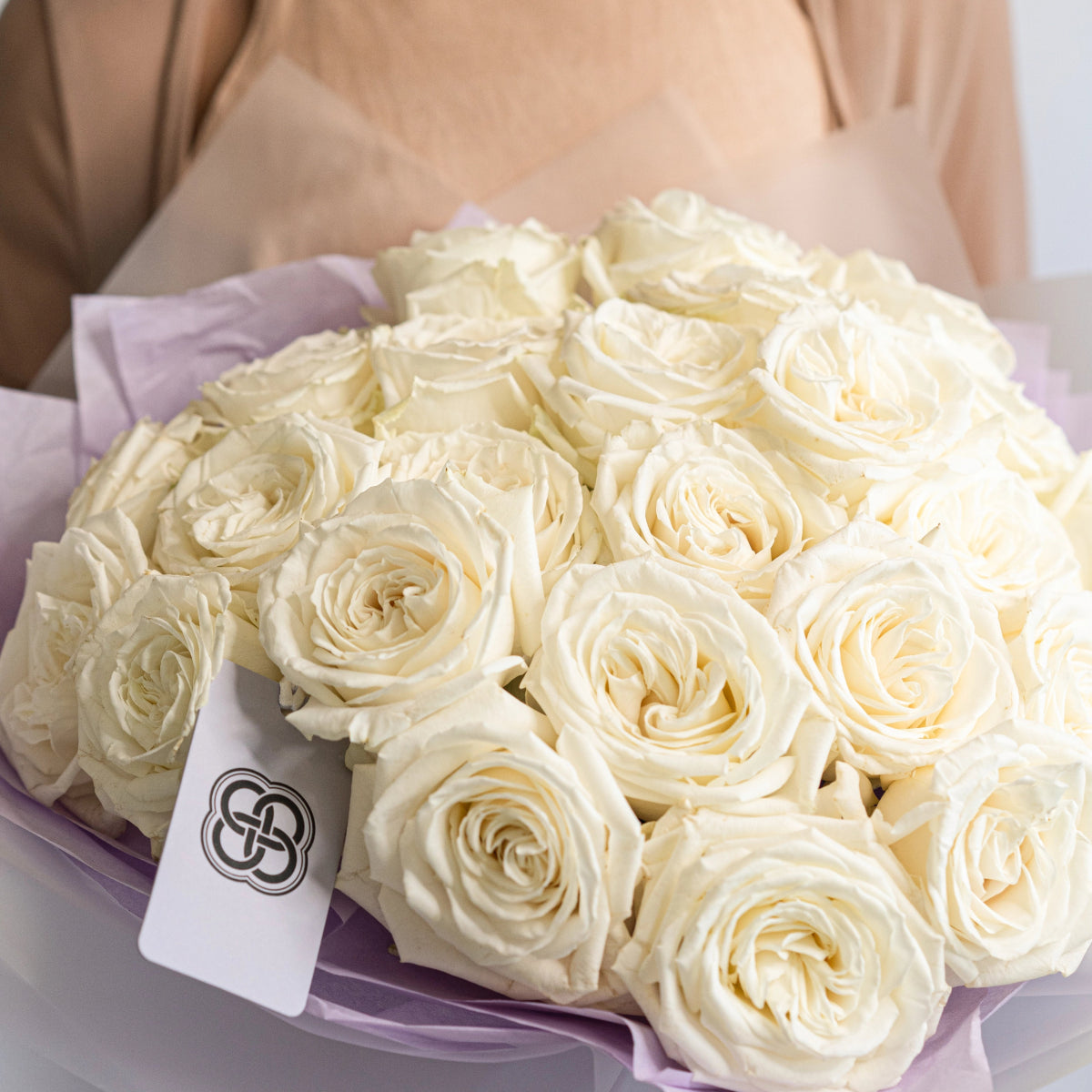 Elegant bouquet of cream white roses wrapped in lavender tissue paper with branded tag