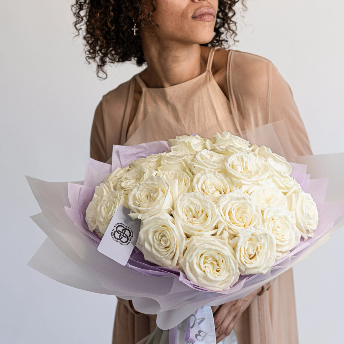 Luxurious bouquet of cream white roses wrapped in lavender and gray tissue paper with brand tag