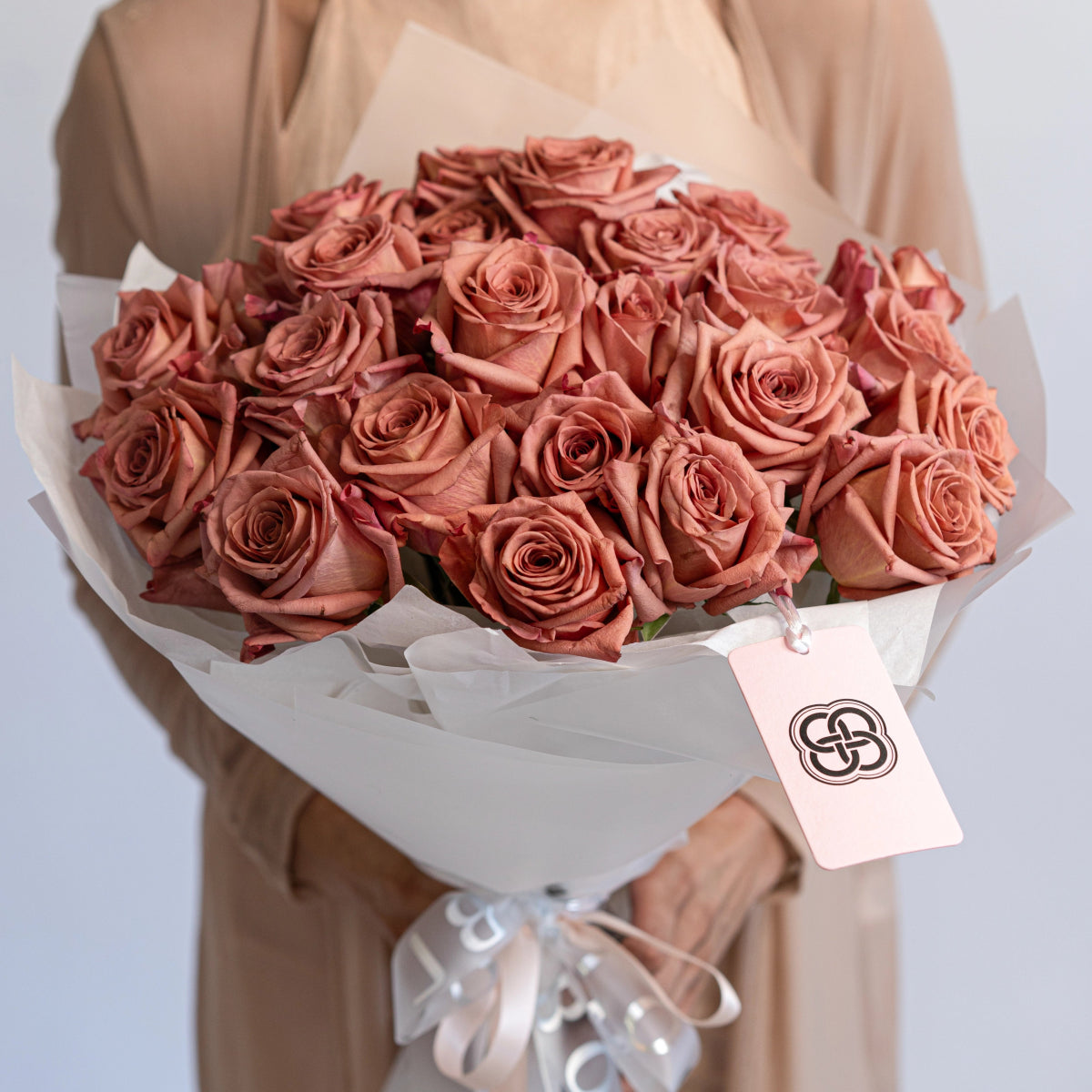 Dusty rose pink roses bouquet in white paper wrapping with ribbon, held by person in beige coat