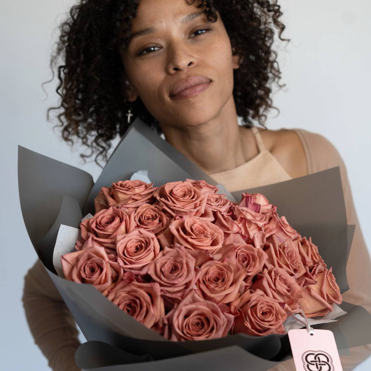 Woman holding large bouquet of dusty rose pink roses wrapped in gray paper with branded tag