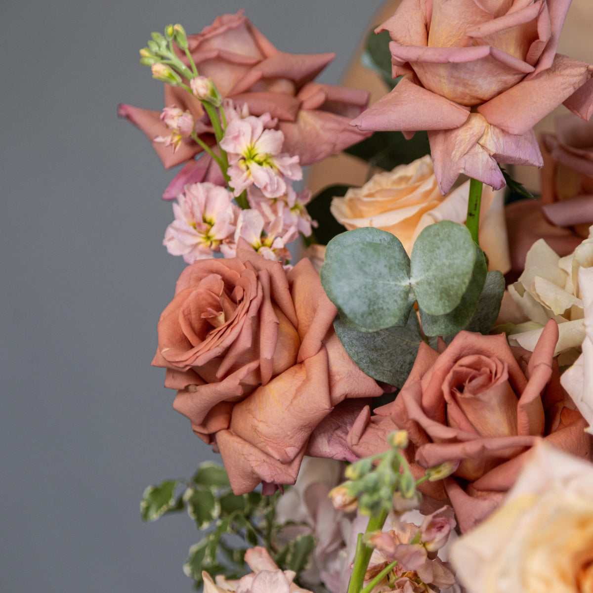 Dusty rose and peach flower bouquet with roses, eucalyptus leaves, and delicate pink blooms on gray background