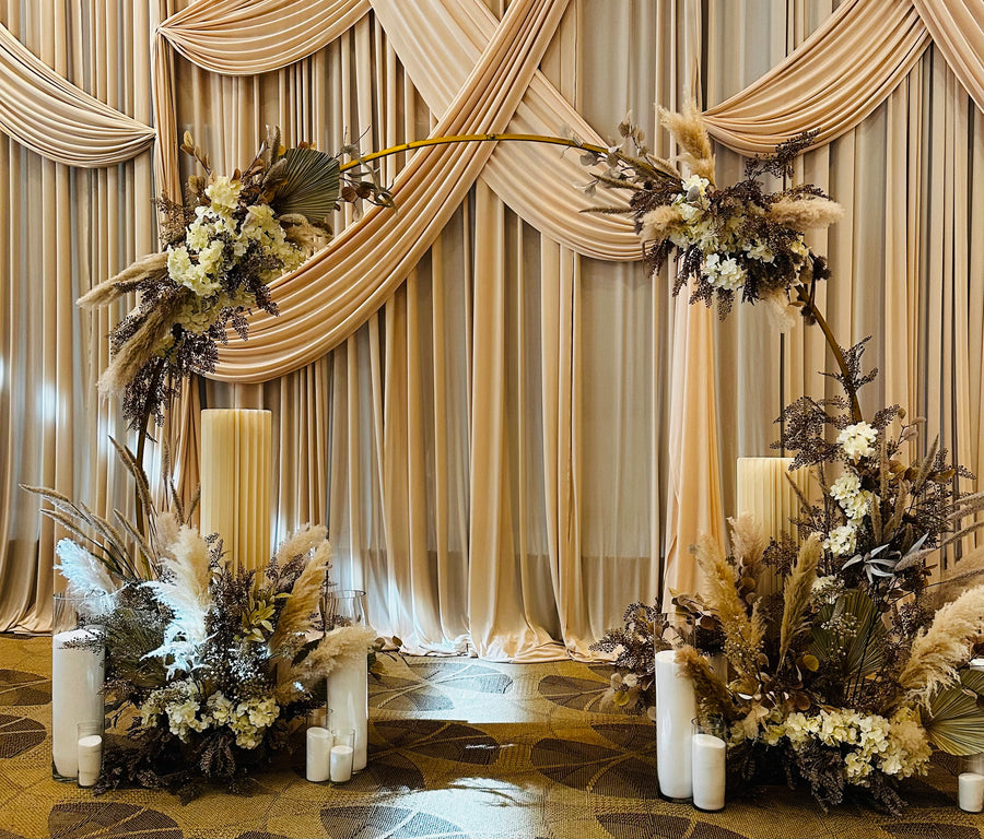 Gold hoop arch dressed in pampas, dried palms and white hydrangea against champagne draping, with candle clusters — bat mitzvah install by Bloom Boom