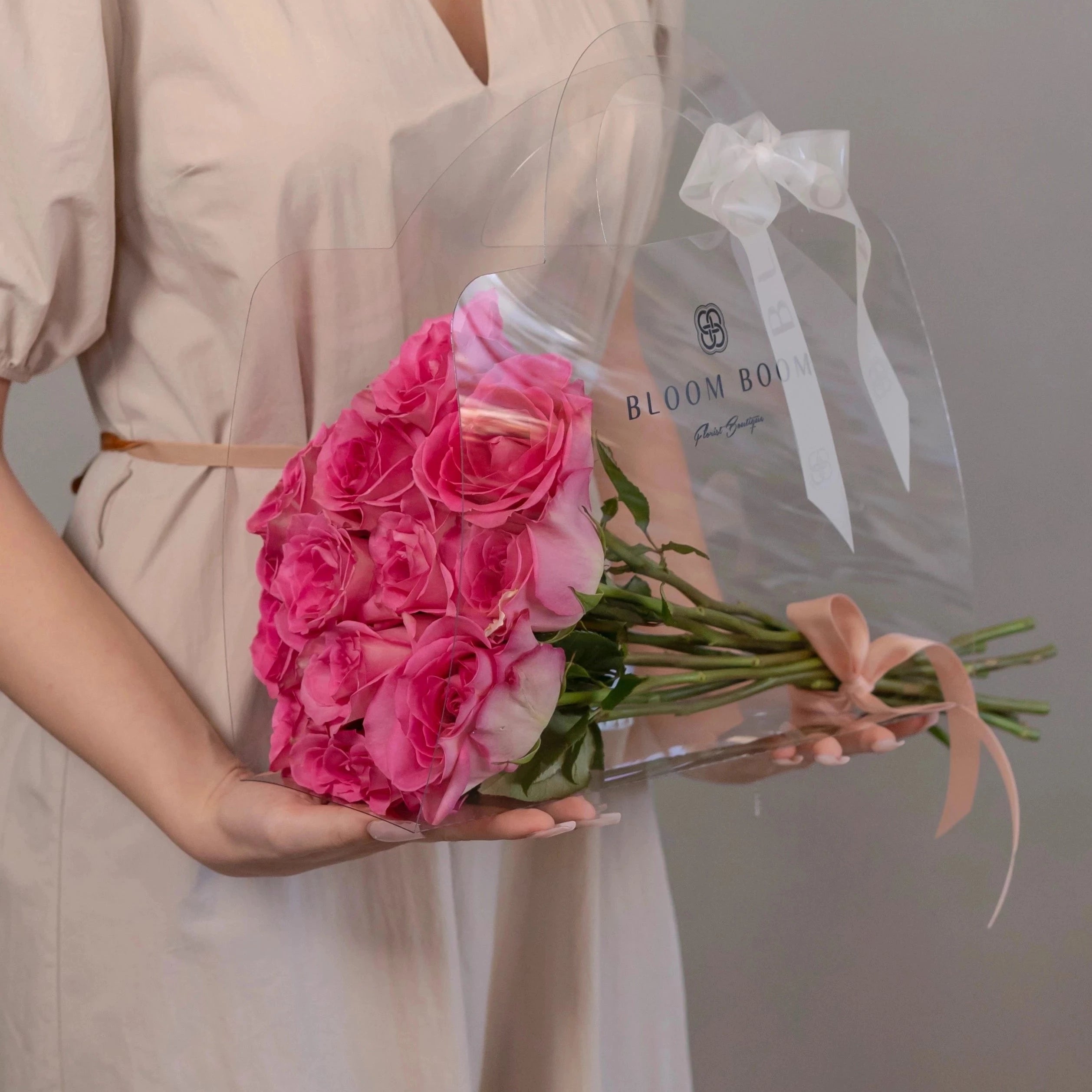 Hot pink roses bouquet in clear cellophane wrap with Bloom Boom branding, tied with pink ribbon