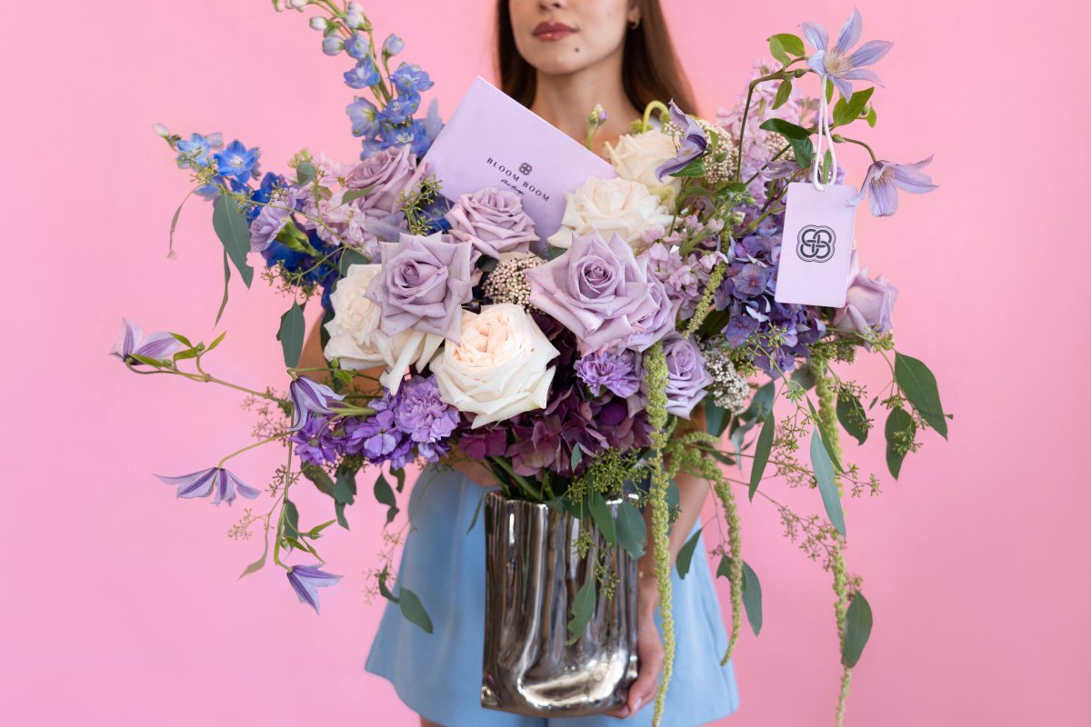 Luxury mixed flower bouquet with lavender roses, white roses, blue delphiniums in chrome silver vase on pink backdrop