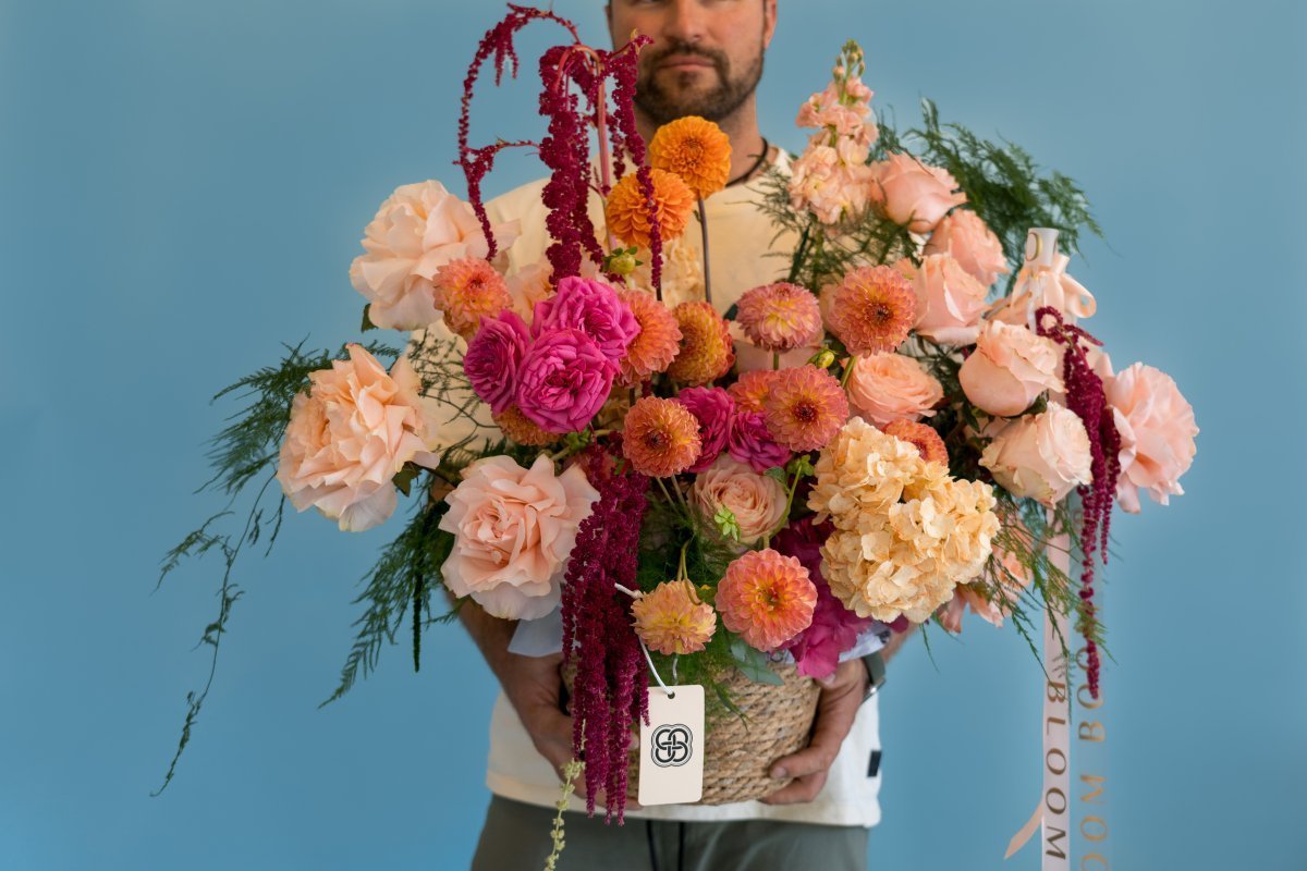 Luxury flower bouquet with peach roses, pink dahlias, orange marigolds and burgundy amaranth in woven basket