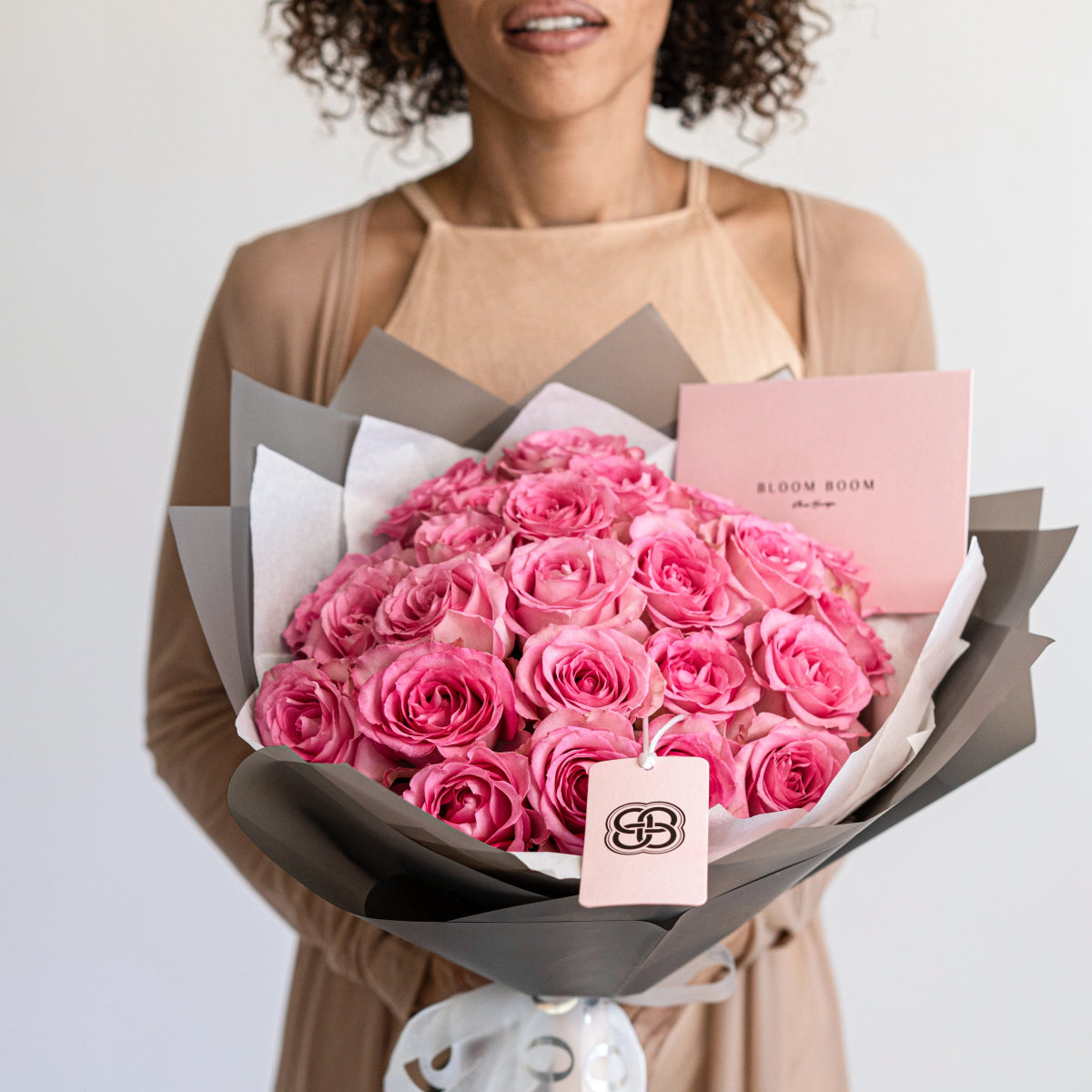 Luxury bouquet of 25 pink roses wrapped in gray and white paper with branded cards held by smiling woman