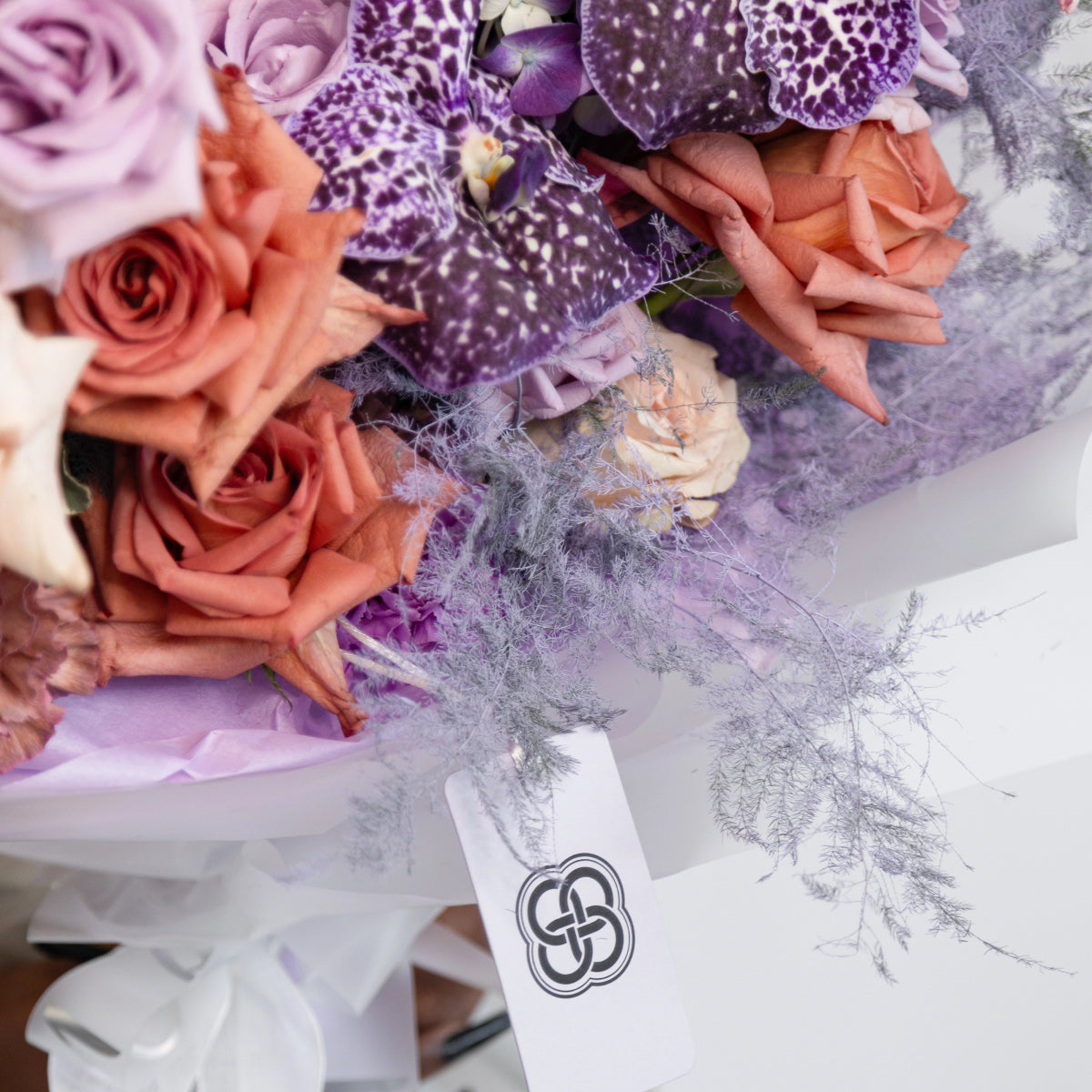 Mixed flower bouquet with coral roses, purple spotted orchids, and white flowers wrapped in soft tulle