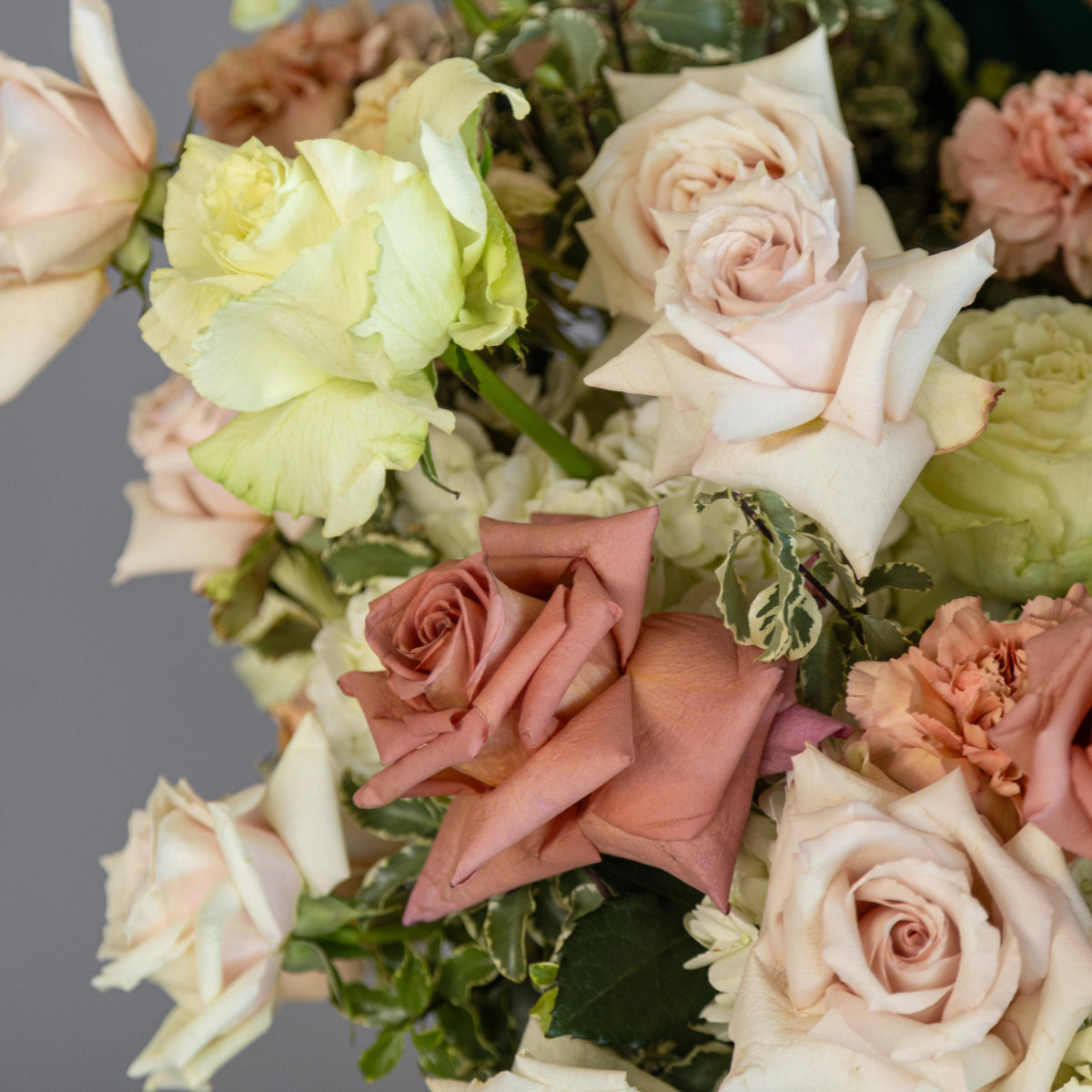 Mixed flower bouquet with blush pink roses, pale green hydrangeas, coral carnations and variegated foliage