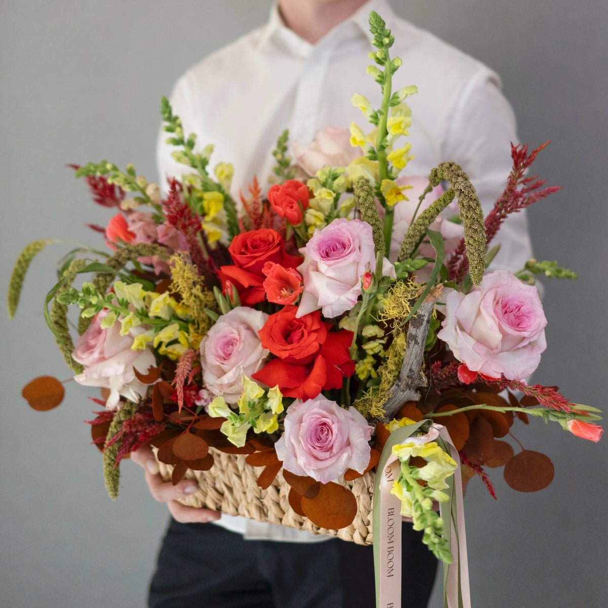 Wicker basket arrangement with red and pink roses, green amaranthus, yellow snapdragons, and burgundy foliage