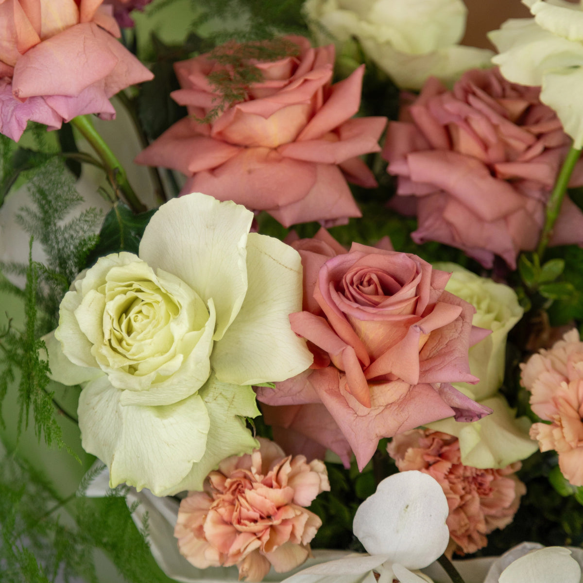 Mixed flower bouquet with white roses, coral pink roses, peach carnations and green foliage arrangement