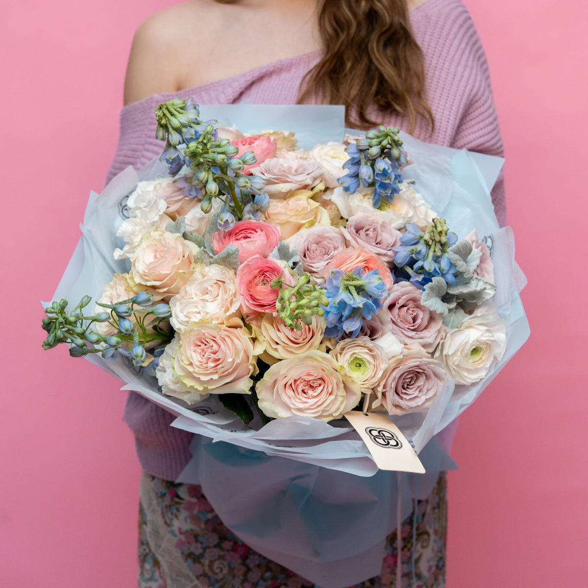 Mixed flower bouquet with blush pink roses, coral ranunculus, blue delphiniums wrapped in translucent paper