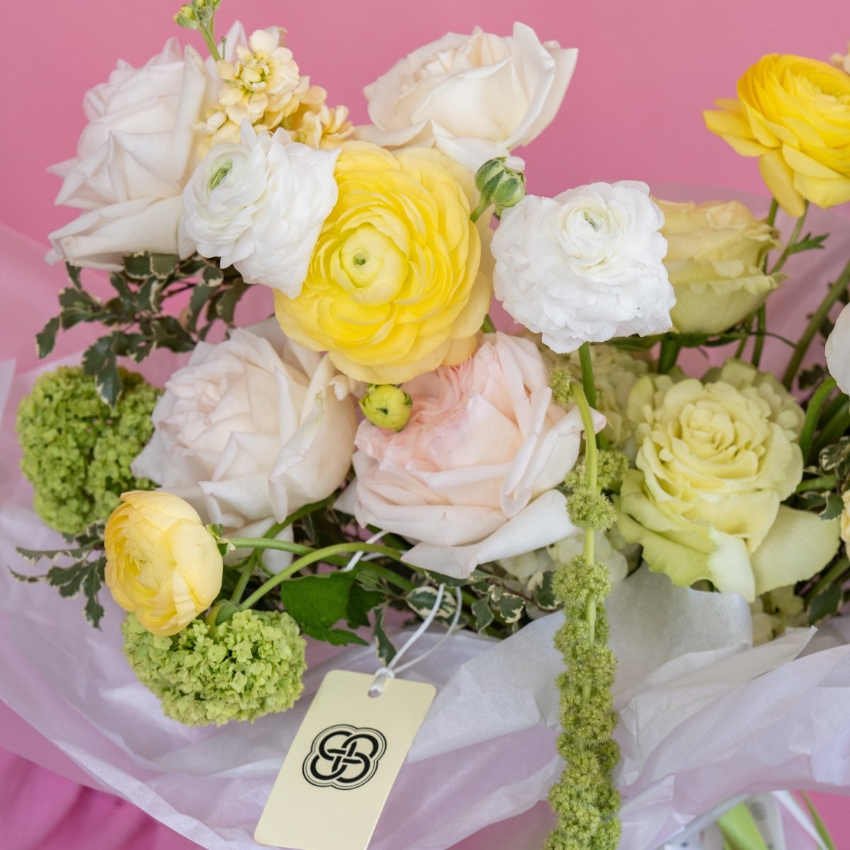 Mixed spring bouquet with yellow ranunculus, white and blush pink flowers, green viburnum in clear cellophane wrap