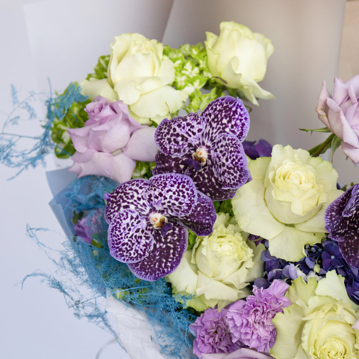 Mixed flower bouquet with purple spotted orchids, white roses, lavender lisianthus and blue sisal wrapping