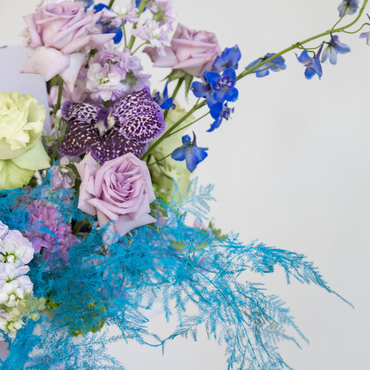 Mixed flower bouquet with lavender roses, purple spotted orchids, blue delphiniums, and turquoise dried ferns