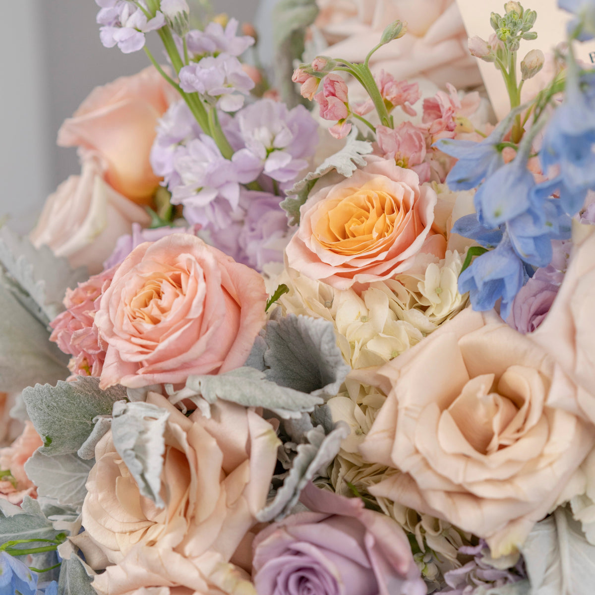 Pastel flower bouquet with peach roses, lavender stock flowers, blue delphinium and dusty miller foliage