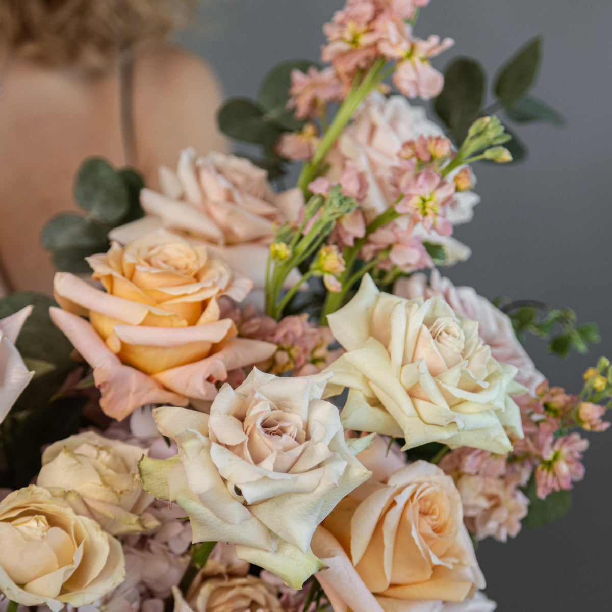Soft pastel flower bouquet with cream and peach roses, pink stock flowers, and eucalyptus leaves