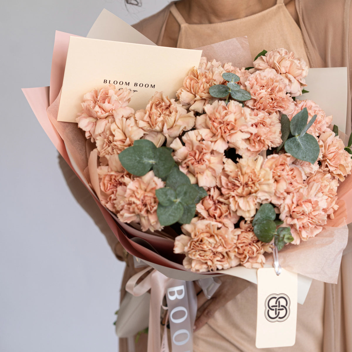 Peach carnation bouquet with eucalyptus leaves wrapped in cream paper with Bloom Boom branding