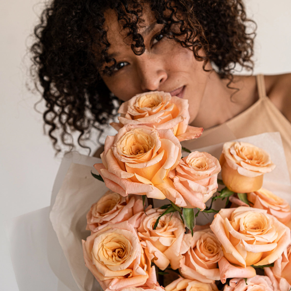 Woman holding bouquet of peach and coral colored roses with soft gradient petals and green foliage