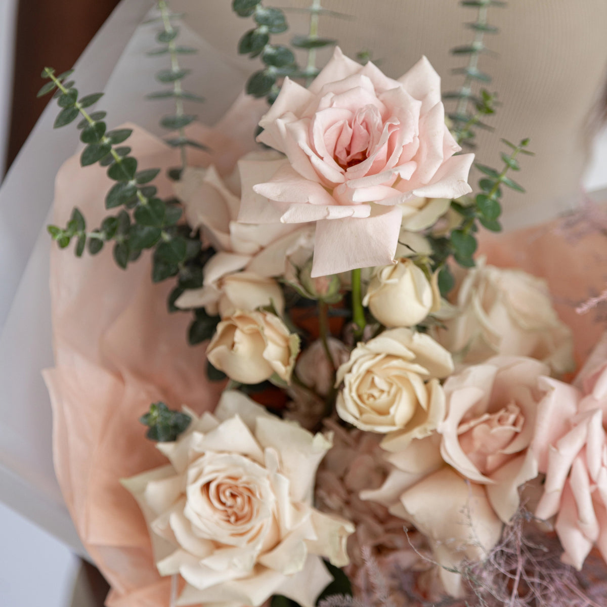 Soft pink and cream rose bouquet with eucalyptus wrapped in blush pink paper packaging