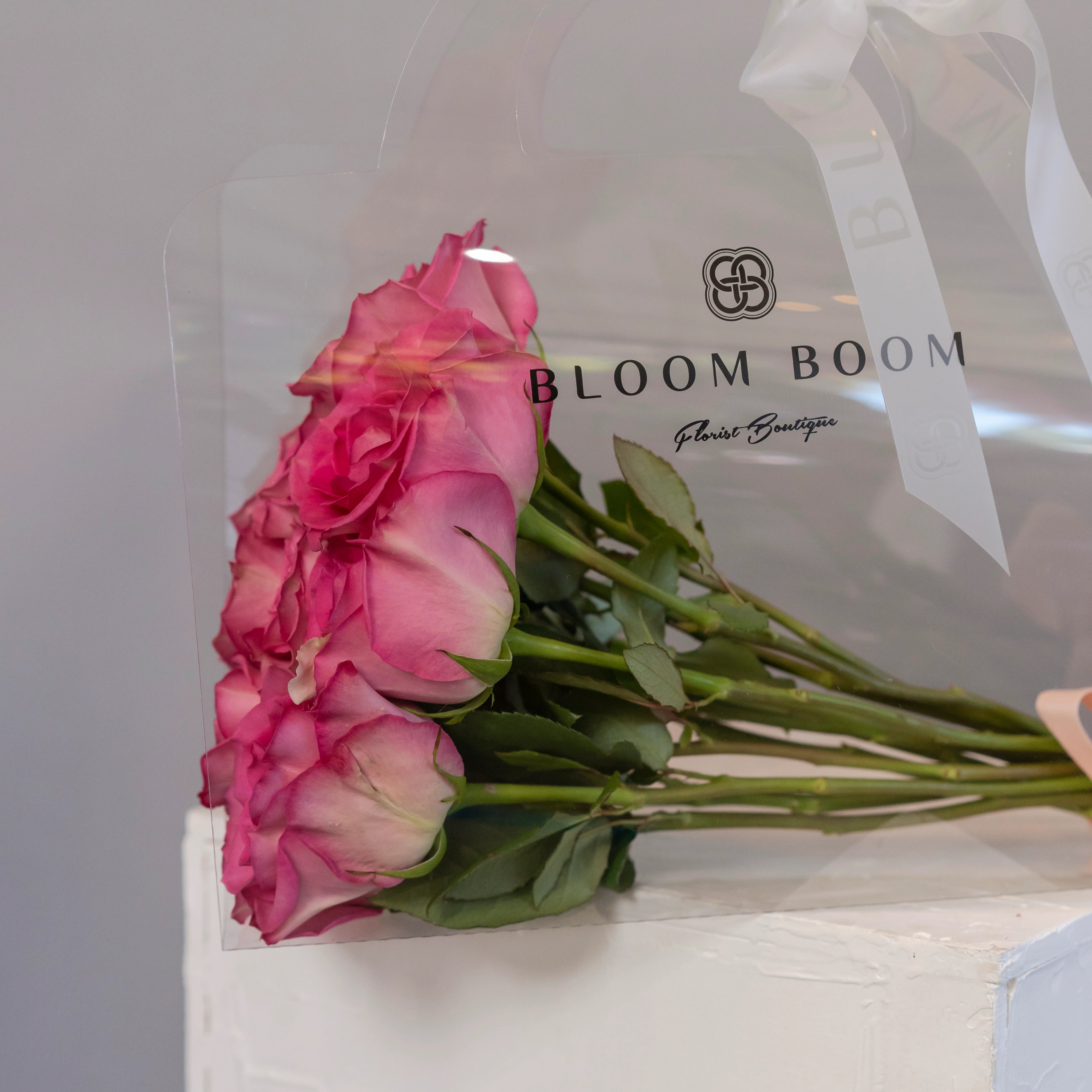 Pink rose bouquet in clear Bloom Boom Florist Boutique bag with white ribbon handles for flower delivery