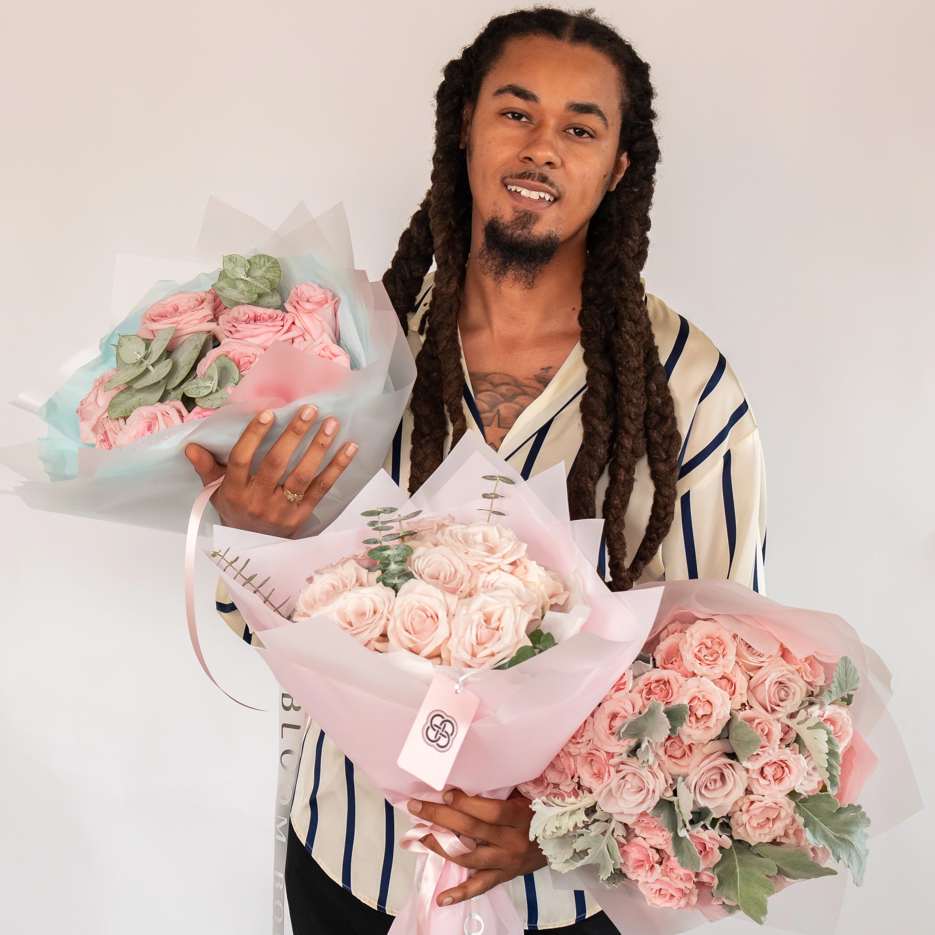 Three pink rose bouquets in mint, white and pink wrapping with eucalyptus leaves held by smiling delivery person