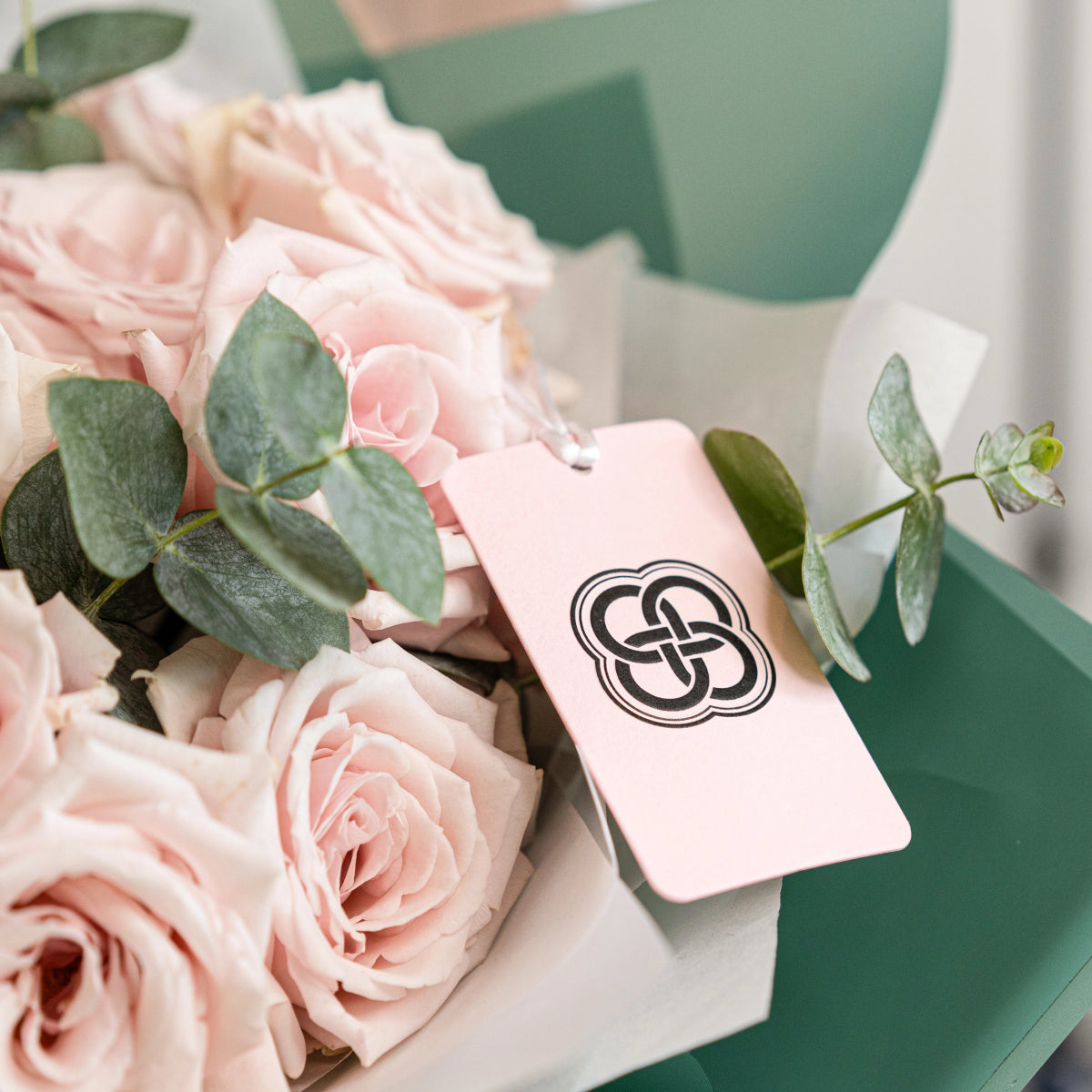 Pink rose bouquet with eucalyptus leaves and branded gift tag in white wrapping with sage green ribbon