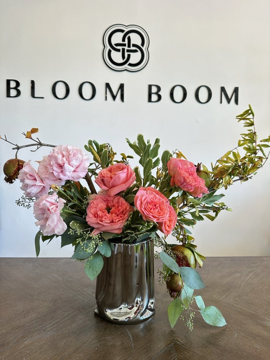 Pink rose and carnation bouquet in clear glass vase with eucalyptus greenery on wooden surface