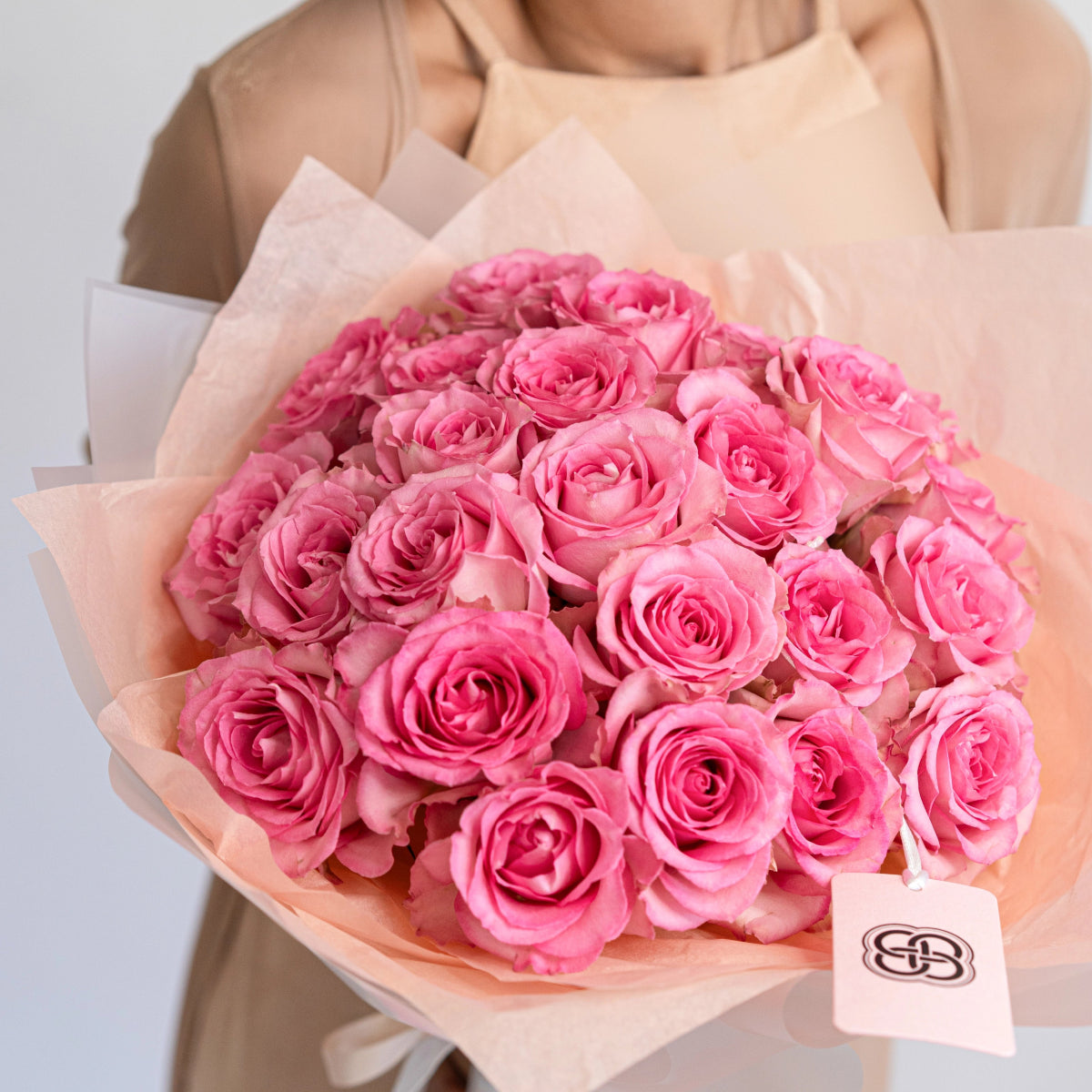 Elegant bouquet of 25 pink roses wrapped in soft peach tissue paper with brand tag
