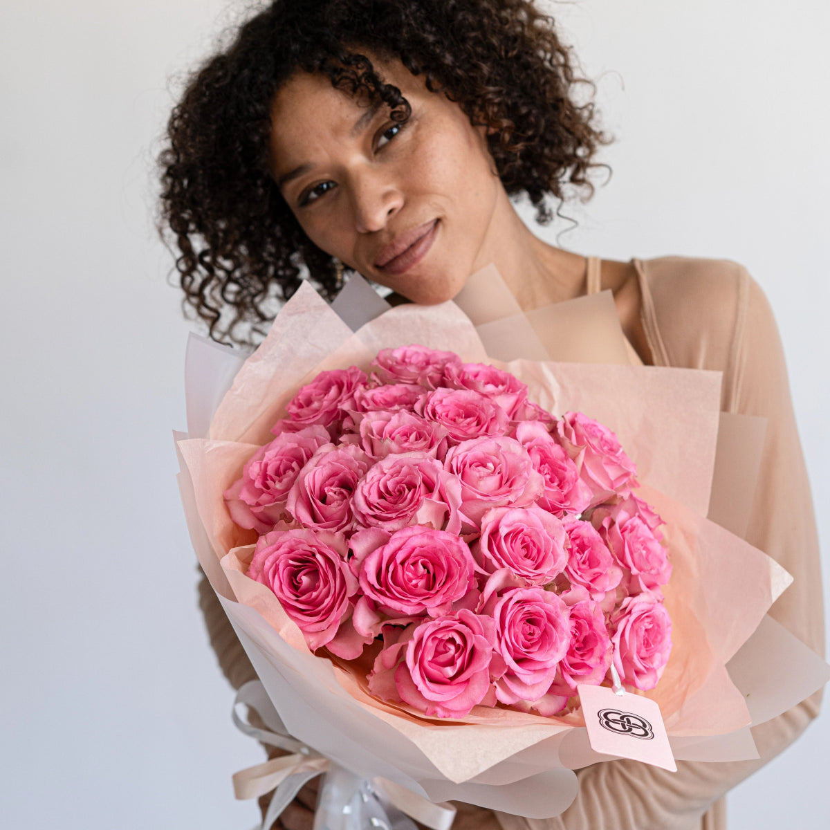 Pink roses bouquet wrapped in blush tissue paper held by woman with curly hair in beige top