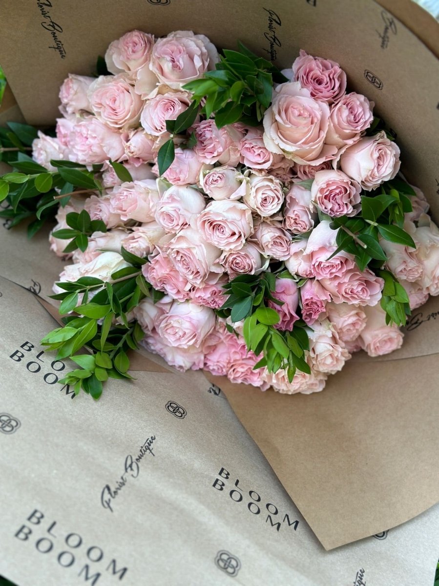 Fresh pink roses and carnations bouquet with green foliage wrapped in kraft paper packaging