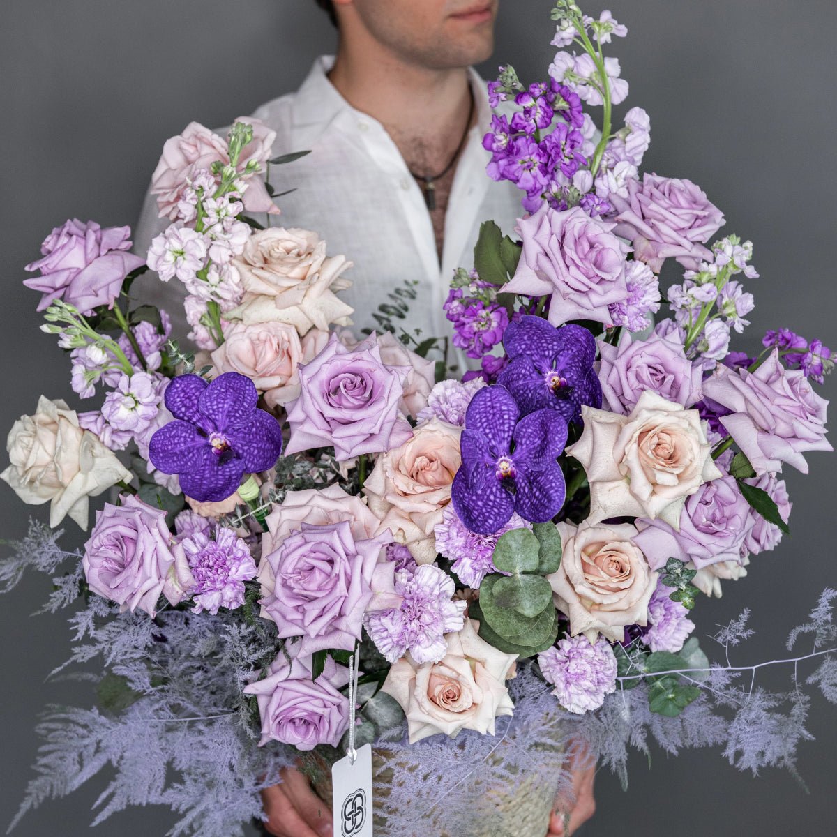 Purple Bliss flower box with lavender roses, purple orchids, dusty miller and mixed blooms in white textured container