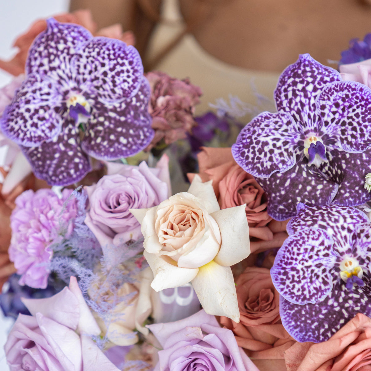 Purple spotted orchids with cream, lavender and peach roses in elegant floral arrangement bouquet