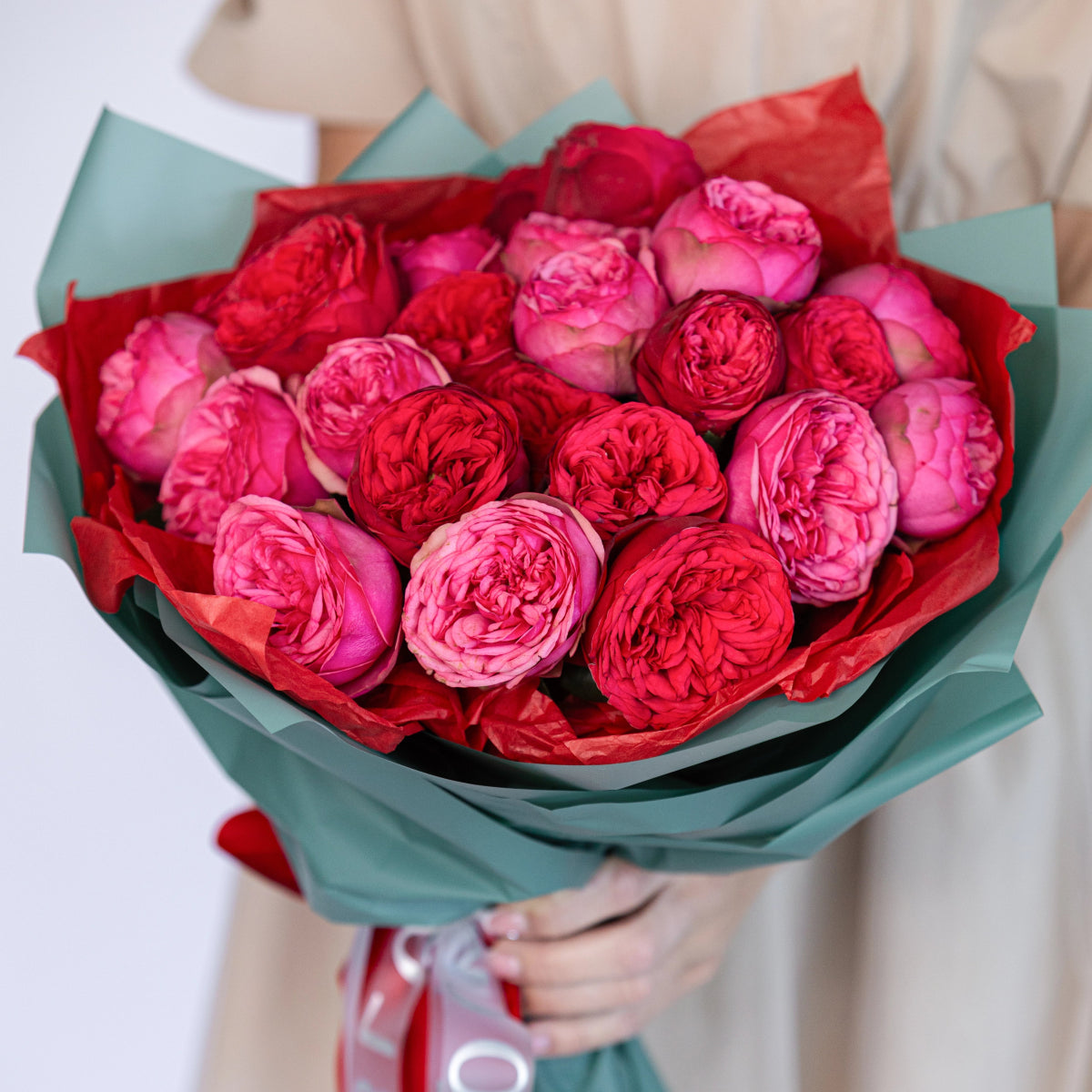 Luxurious bouquet of red and pink garden roses with ruffled petals wrapped in mint green and red tissue paper