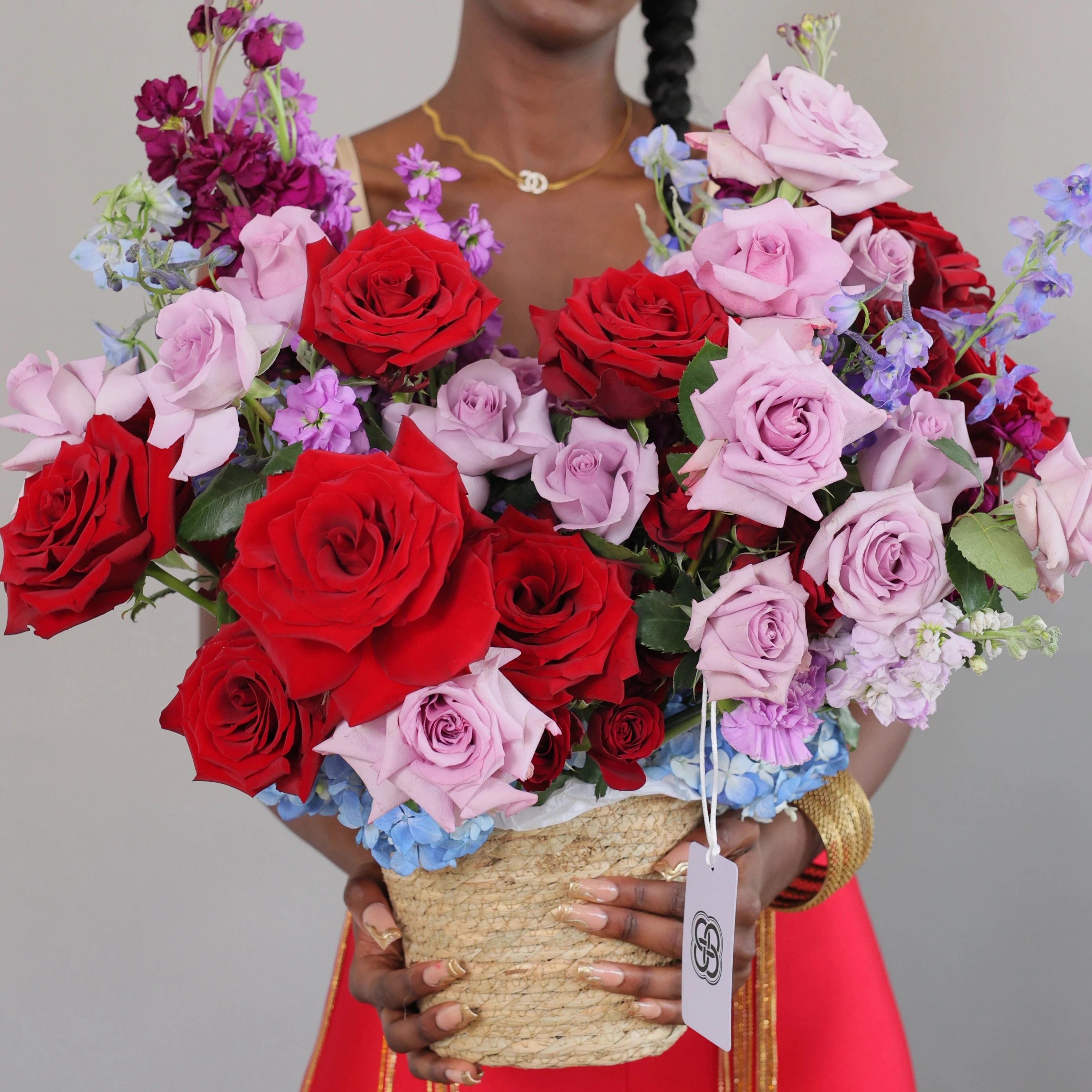 Mixed rose basket arrangement with red and pink roses, purple stock, blue delphinium in woven basket - Los Angeles florist
