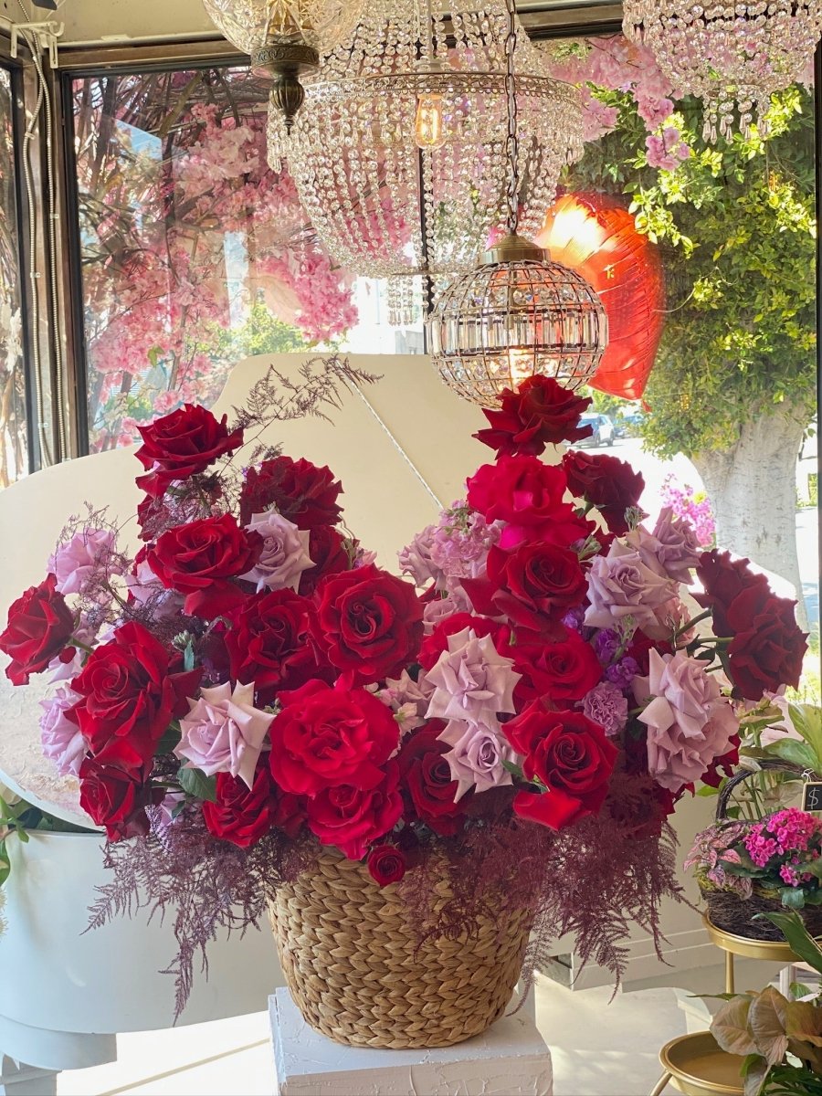 Wicker basket filled with deep red and lavender purple roses with decorative fern accents in bright flower shop