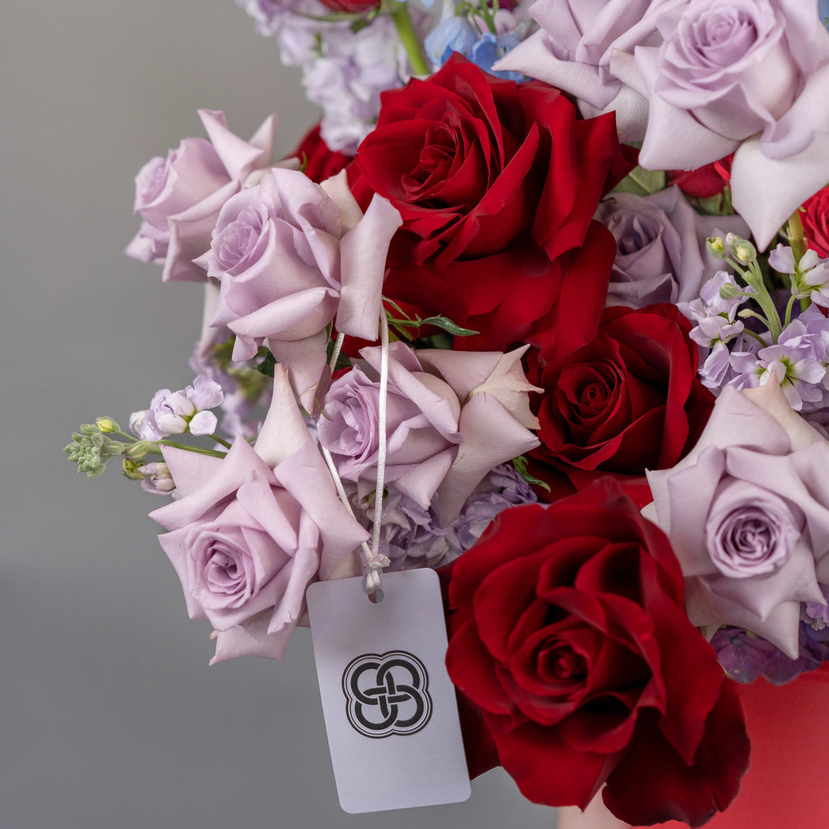 Mixed rose bouquet with deep red and lavender purple roses, white filler flowers, branded white gift tag
