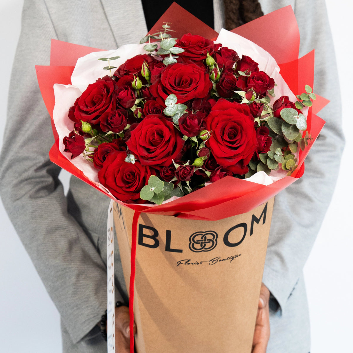 Red rose bouquet with eucalyptus in coral paper wrapping held in brown Bloom Florist Boutique shopping bag