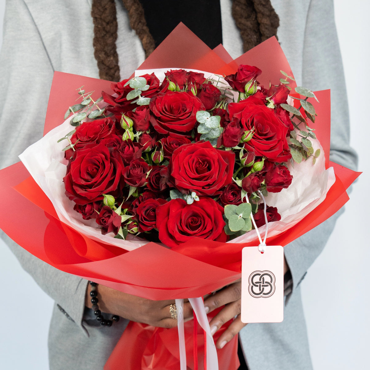 Elegant red rose bouquet with eucalyptus wrapped in coral paper with gift tag held by person in white coat