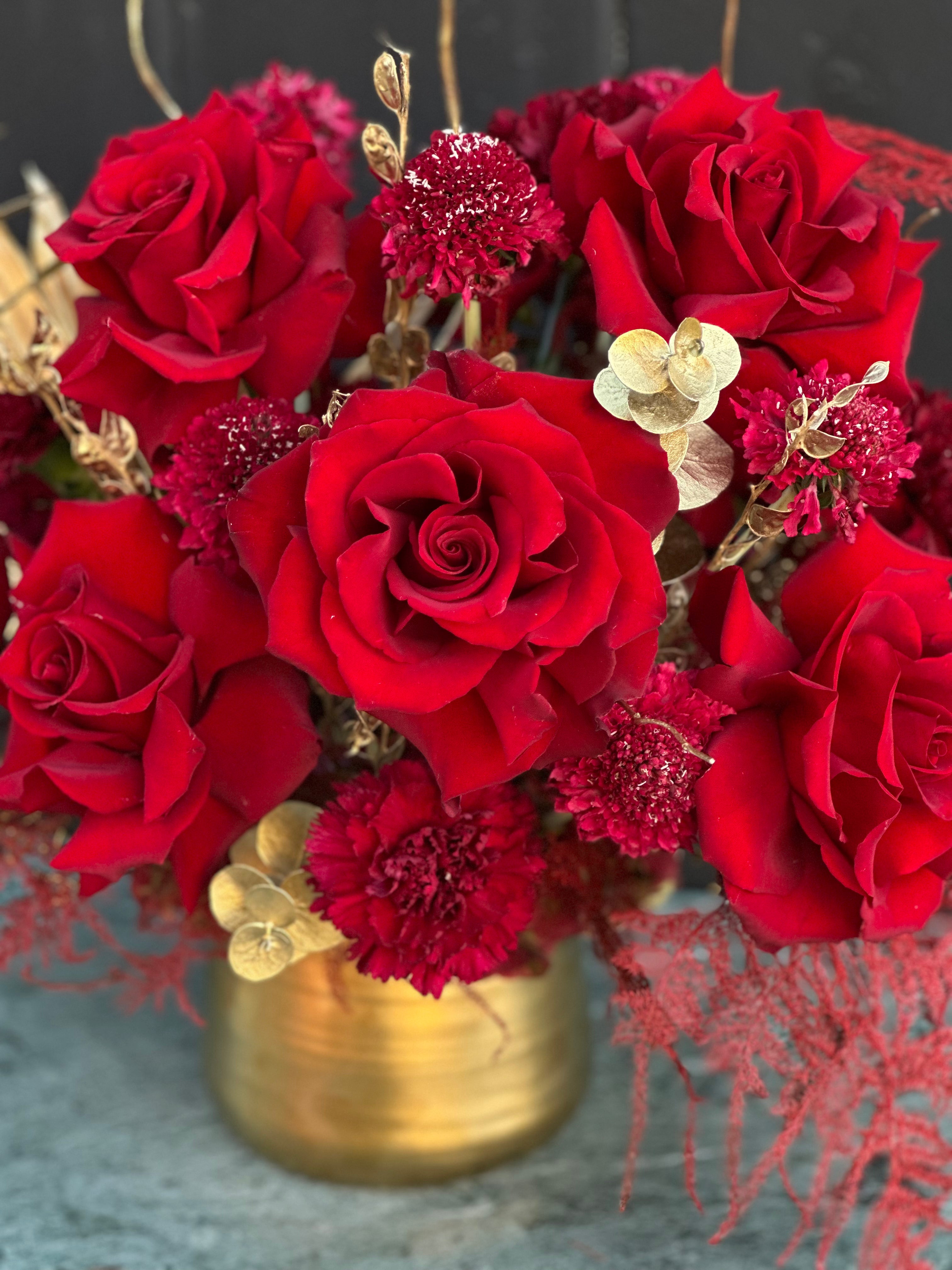 Red roses and burgundy chrysanthemums with golden eucalyptus leaves arranged in brass vase