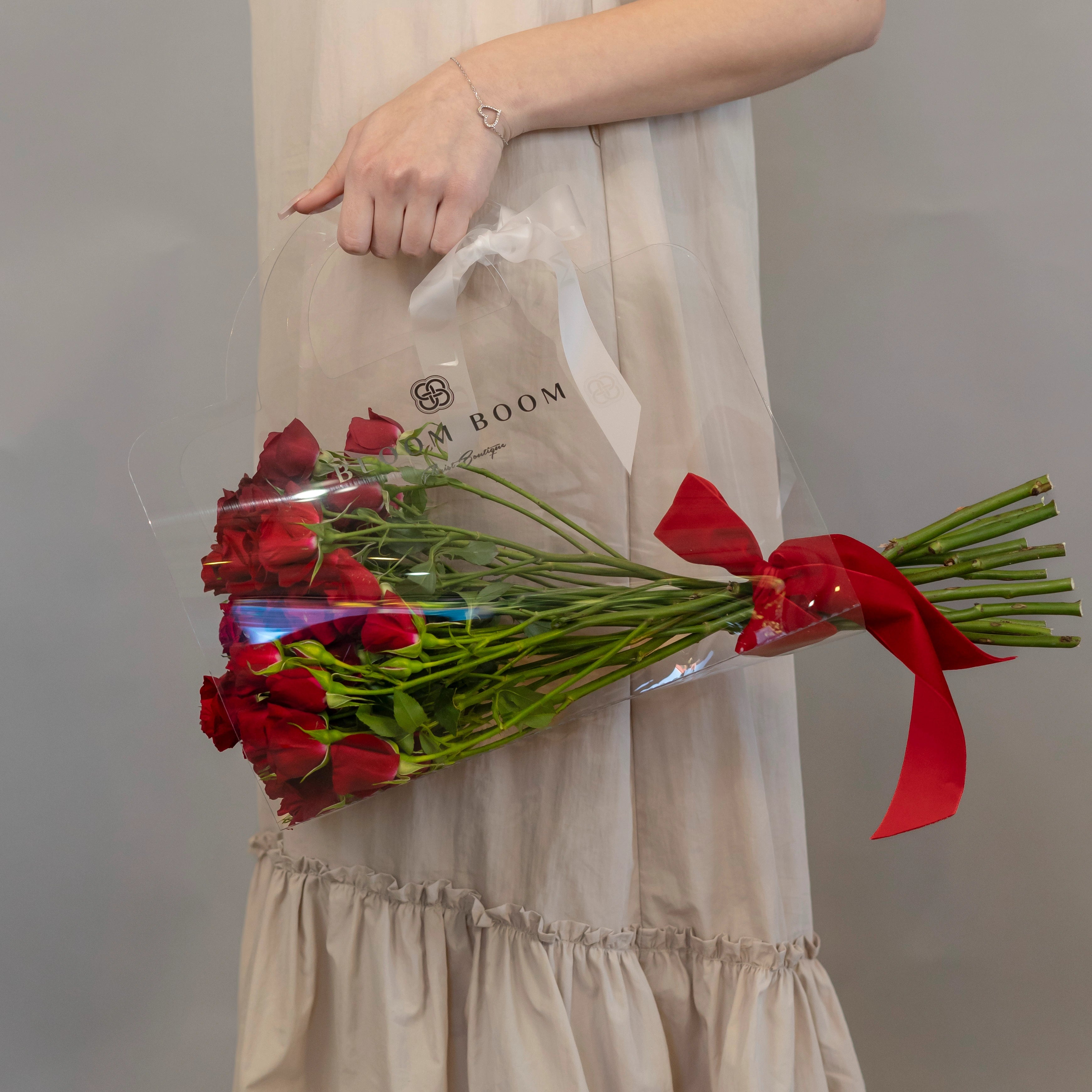 Red roses bouquet with cellophane wrap and red ribbon next to Bloom Boom florist delivery bag in Los Angeles