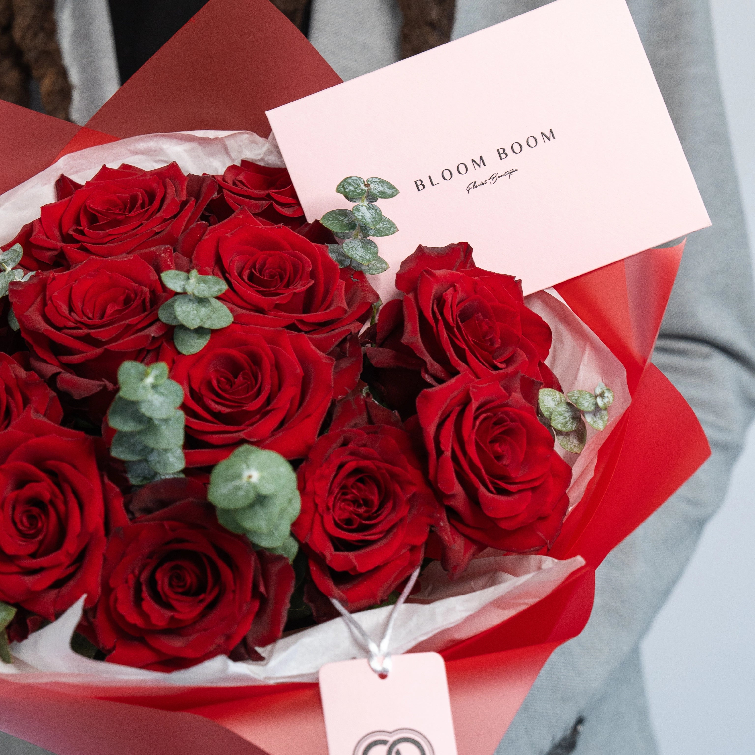 Red roses bouquet with eucalyptus in red white wrapping featuring Bloom Boom Flowers branded card Los Angeles florist