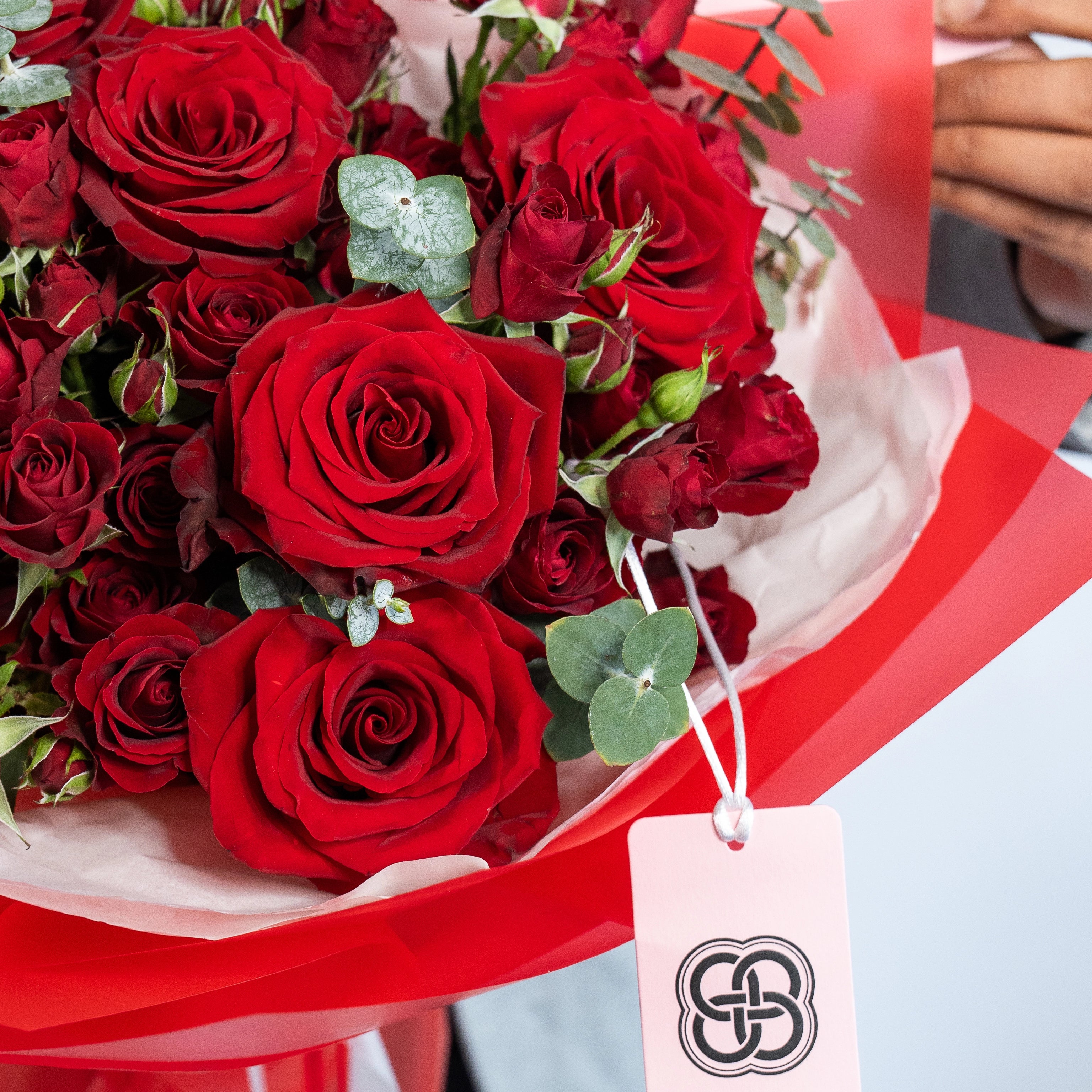 Red roses bouquet with eucalyptus leaves wrapped in white paper with red ribbon and gift tag for Valentine's Day