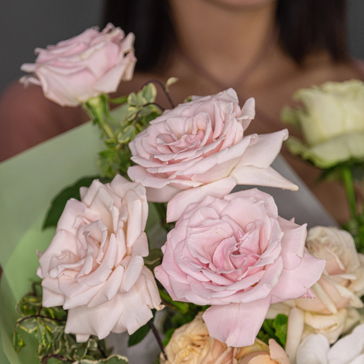 Soft pink roses with green leaves in mixed flower bouquet arrangement with cream and white blooms