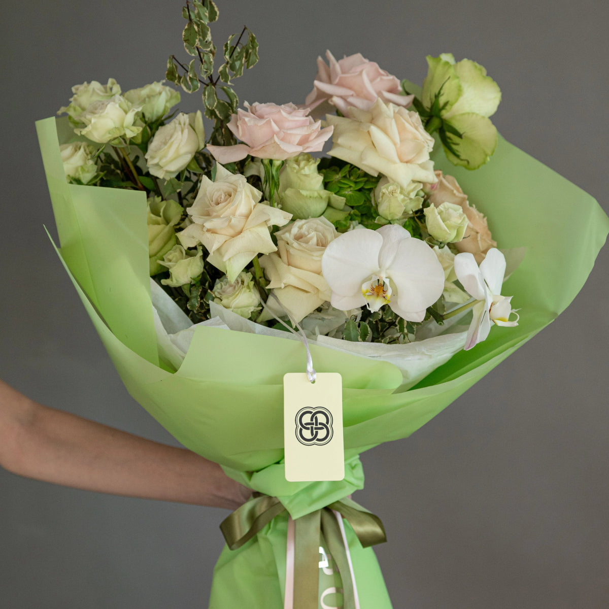 Mixed flower bouquet with cream roses, white orchids, green hydrangeas in lime green wrapping paper with ribbon