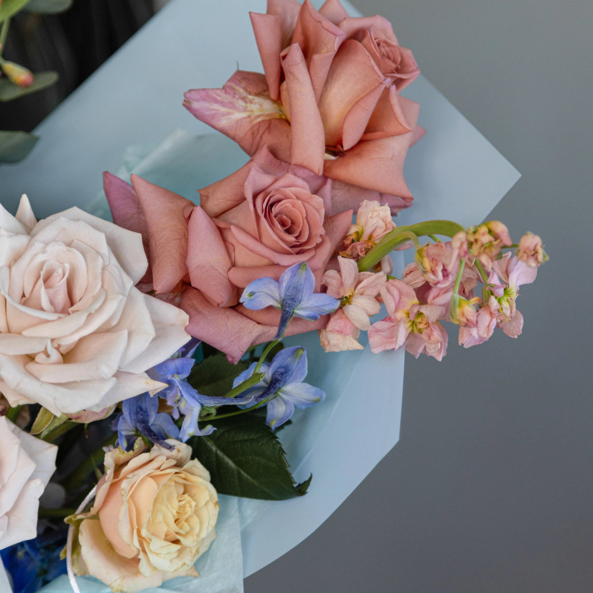 Vanilla Sky bouquet with blush pink roses, white roses, blue delphiniums and pink hydrangeas wrapped in blue paper